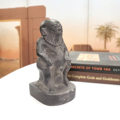 Statue of a seated stone statue of the Egyptian God Bes figure with a desert scene in the background