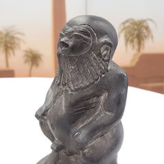 Statue of a bearded stone statue of the Egyptian God Bes figure with a desert landscape in the background