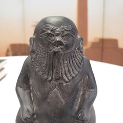 Statue of a bearded stone statue of the Egyptian God Bes figure with a fish on a plain background