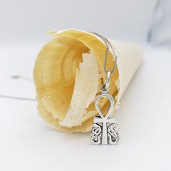 Silver an ankh and cobra charm on a chain with a shell in the background