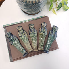 Decorative items resembling ancient Egyptian mummies on a book with a plant in the background