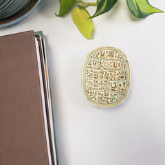 Decorative round scarab object with intricate patterns on a white surface next to a plant