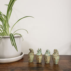 Decorative green canopic jar statues on a wooden door with a plant in the foreground.