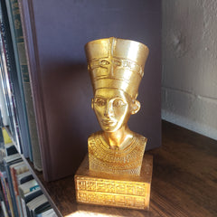 Gold bust of a historical figure on a wooden shelf with books in the background