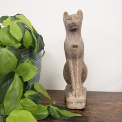 Decorative stone cat sculpture on a wooden surface with green plants in the foreground