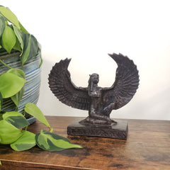 Decorative Egyptian Isis statue on a wooden surface with plants in the background