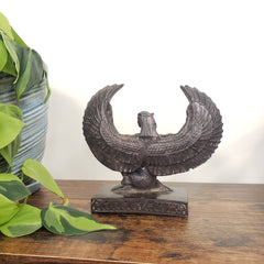 Decorative Egyptian Isis statue on a wooden surface with plants in the foreground