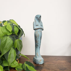 Decorative Egyptian god Horus statue on a wooden surface with green leaves in the foreground