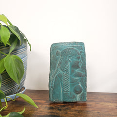 Decorative Cleopatra wall hanging on a white wall with plants in the foreground