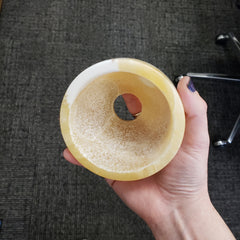 Hand holding a beige alabaster votive holder on a dark textured surface