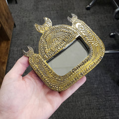 Decorative gold mirror held by a hand against a blurred background