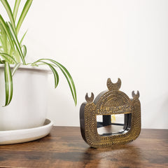 Decorative brass framed mirror on a wooden surface with a plant in the foreground
