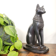 Black Egyptian cat goddess Bastet statue on a wooden surface with green leaves in the foreground