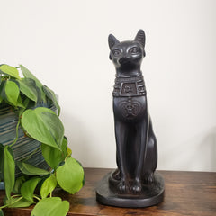 Decorative Black Egyptian cat goddess Bastet statue on a wooden surface with a plant in the foreground.