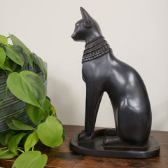 Decorative Black Egyptian cat goddess Bastet statue with a plant in the foreground.