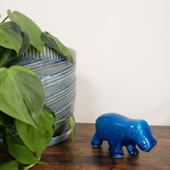 Blue hippo figurine on a wooden surface with green leaves in the foreground
