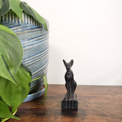 Decorative black cat statue on a wooden surface with green leaves and striped fabric in the background.