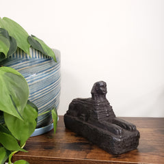 Decorative Egyptian sphinx mounted on a wooden board with plants and a striped pillow in the foreground.