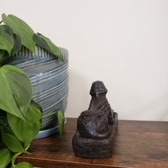 Decorative Egyptian sphinx sculpture on a wooden shelf with plants in the foreground