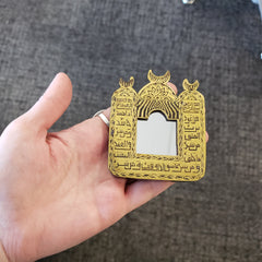 Gold decorative item with Arabic text held in a hand against a textured gray background