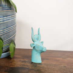 Turquoise Egyptian goddess Hathor bust statue on a wooden surface with a white wall background
