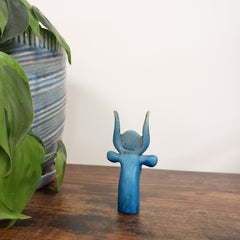 Blue Egyptian goddess Hathor bust statue on a wooden surface with green plants and a striped fabric in the background.