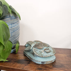 Decorative Egyptian scarab statue with a wooden board and plants in the background