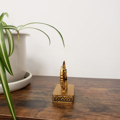 Decorative statue with Egyptian-style design on a wooden surface with a plant in the foreground