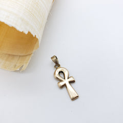 Gold ankh pendant on a white background with a shell to the left.