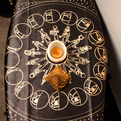 Decorative cloth with astrological symbols and a candle on a black background