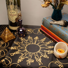 Table with mystical items including a bottle, books, and a candle on a tablecloth with esoteric designs.