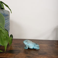 Blue frog figurine on a wooden surface with a plant in the background