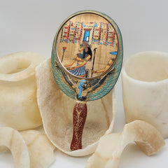 Decorative hand mirror with Egyptian-themed design on a textured surface