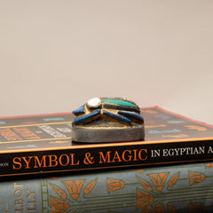Decorative object on top of a book titled 'Symbol & Magic in Egyptian Art' with a plain background.