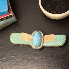 Decorative scarab beetle on a dark surface with books and small bowls in the background