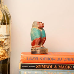 Decorative setup with a bottle, vase, books, and baboon figurine on a table.