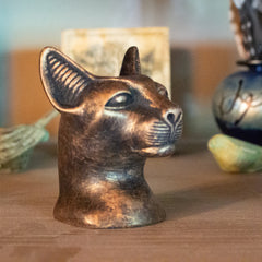 Bronze cat head sculpture on a wooden surface with blurred background