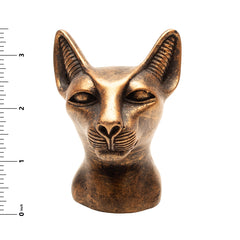 Bronze cat head sculpture with a ruler for scale on a white background