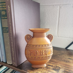 Decorative brown vase with intricate patterns on top of books