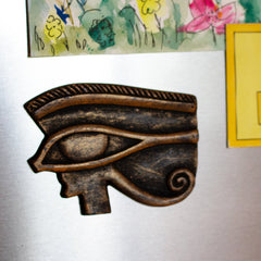 Decorative eye-shaped magnet on a refrigerator with colorful magnets in the background.