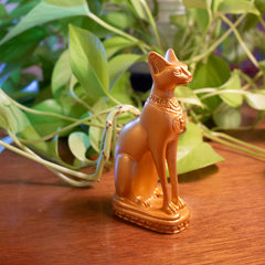 Gold cat figurine on a wooden surface with green plants in the background