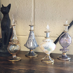 Set of decorative glass bottles on a wooden surface with a black cat figurine in the background.
