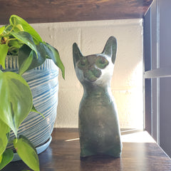 Decorative cat-shaped object on a shelf with plants in the foreground