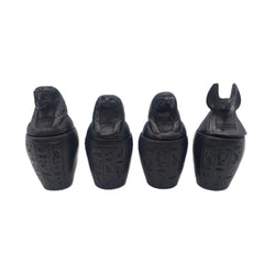 Four black canopic jars with hieroglyphics on a white background