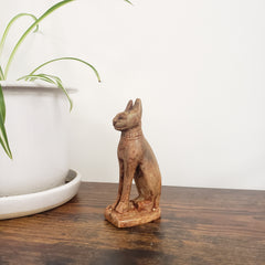 stone sculpture of a cat on a wooden shelf with a plant in the background