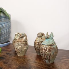 Decorative Egyptian-style canopic jars figurines on a wooden surface with a white background