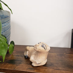 Small beige Decorative stone lion sculpture on a wooden surface with a white wall and plant in the background