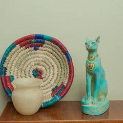 Decorative items including a colorful woven basket, a white vase, and a turquoise cat statue on a wooden surface.