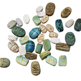 A collection of assorted Egyptian Scarab beads, made of carved soapstone, in various sizes and colors with hieroglyphic symbols on some of them.