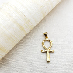 Gold plated ankh pendant next to a white roll of paper on a beige background.
